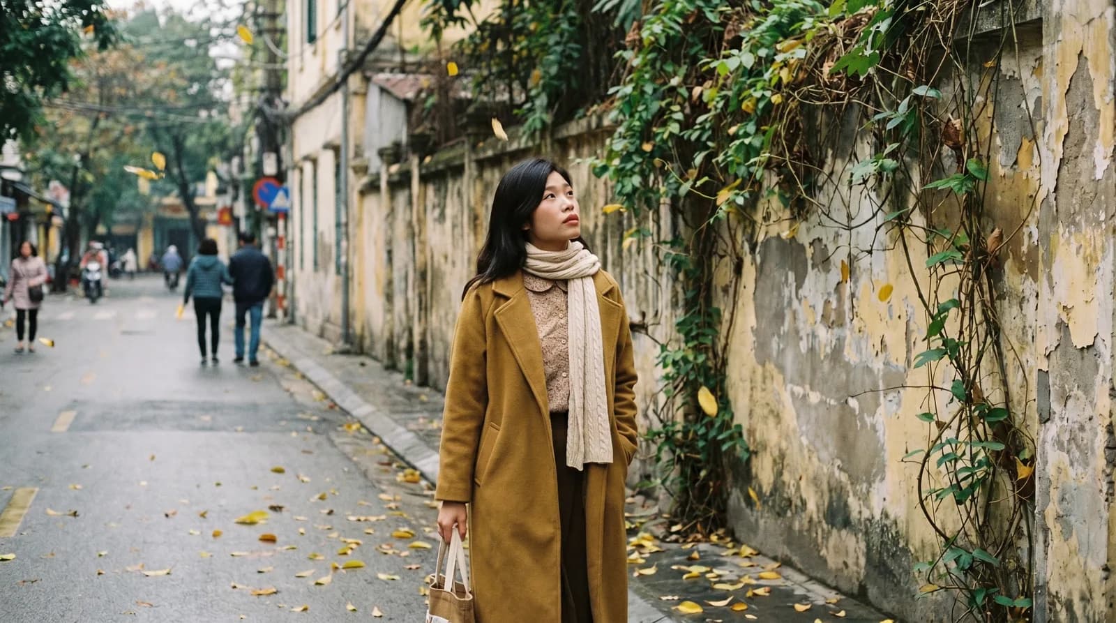 Hà đi bộ qua một bức tường thuộc địa cũ ở phố cổ Hà Nội, mùa thu lá vàng rơi